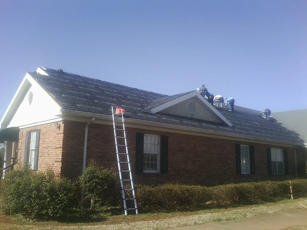 Crew tearing shingles off a brick ranch roof with a ladder set — Emergency Roof Repair work by our crew in Amesbury
