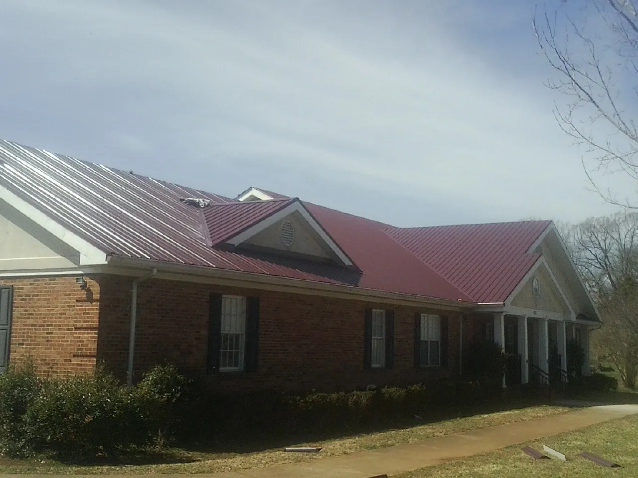 Red metal roof with gabled entries on a long brick building, from a Hail Damage Roof Repair job in Amesbury