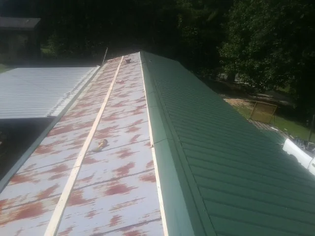 Old rusted panels beside newly installed green metal roofing — Wind Damage Roof Repair by Roofing Brothers in Amesbury
