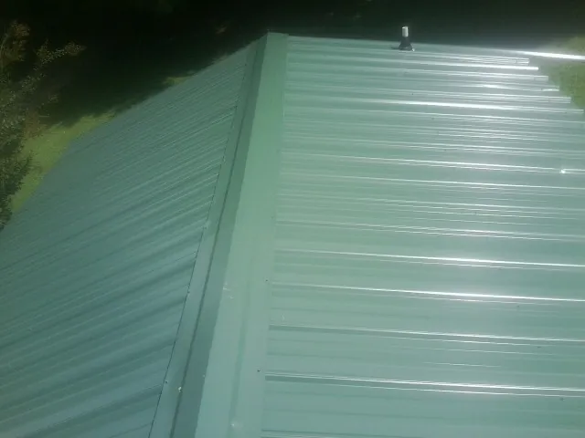 New green metal panels meeting at the ridge of a roof — Flat Roof Repair work by our crew in Amesbury