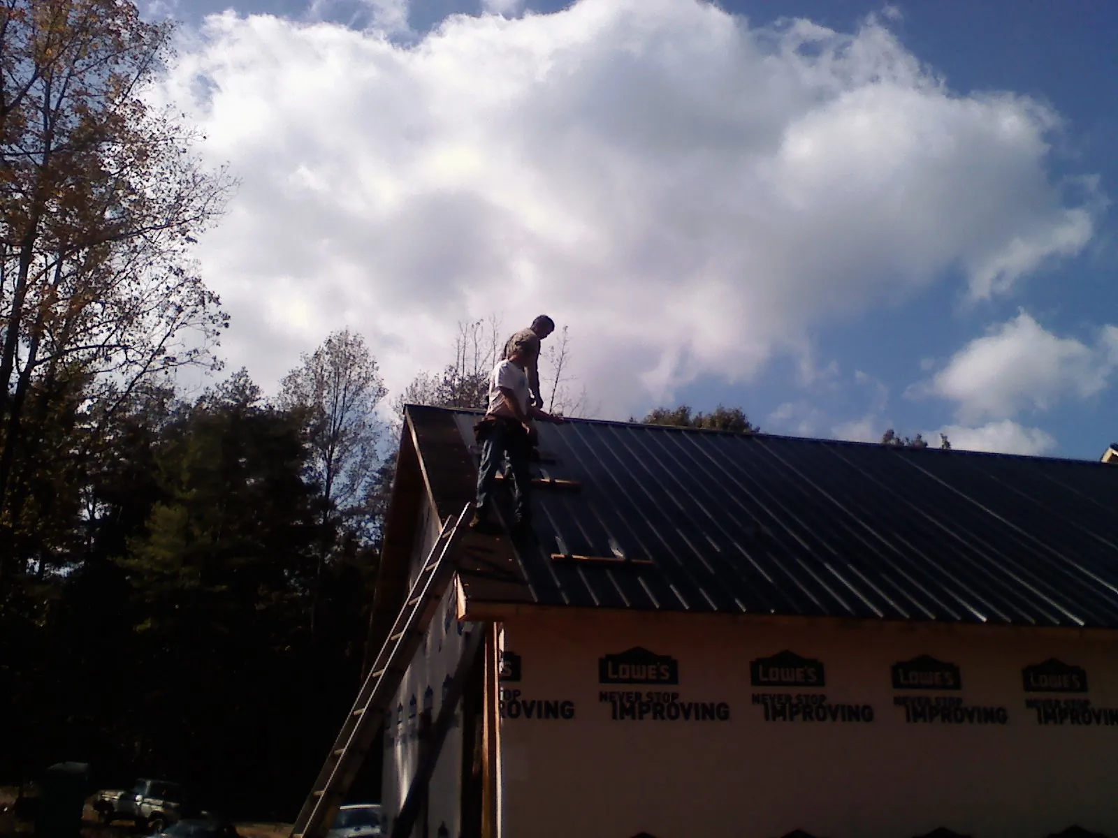 Roofer fastening dark metal panels high against a cloudy sky, from a Roof Inspection job in Amesbury