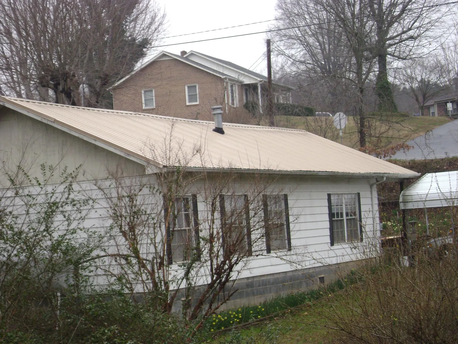 Tan metal roof on a white sided house set into a hillside — Commercial Roofing by Roofing Brothers in Amesbury