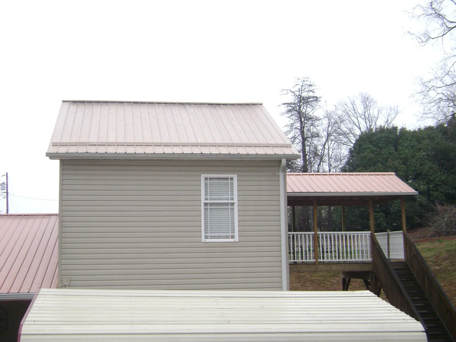 Tan metal roofs on a two story addition and attached porch, from a Roof Replacement job in Amesbury